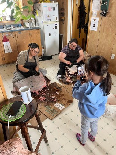 Two women cleaning sealskins as young girl photographs them