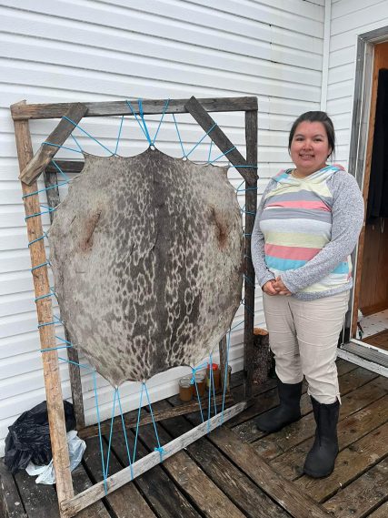 Indigenous girl standing in front of stretched out sealskin