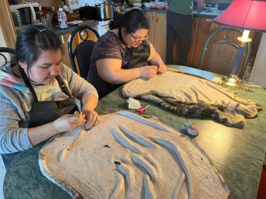Two women with sealskins on a table