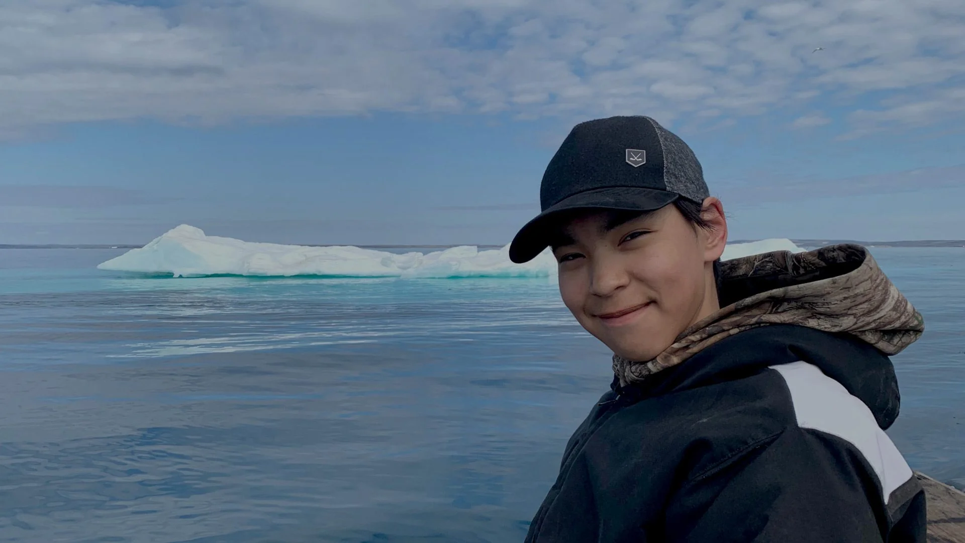 a young indigenous man stands in front of a glacier
